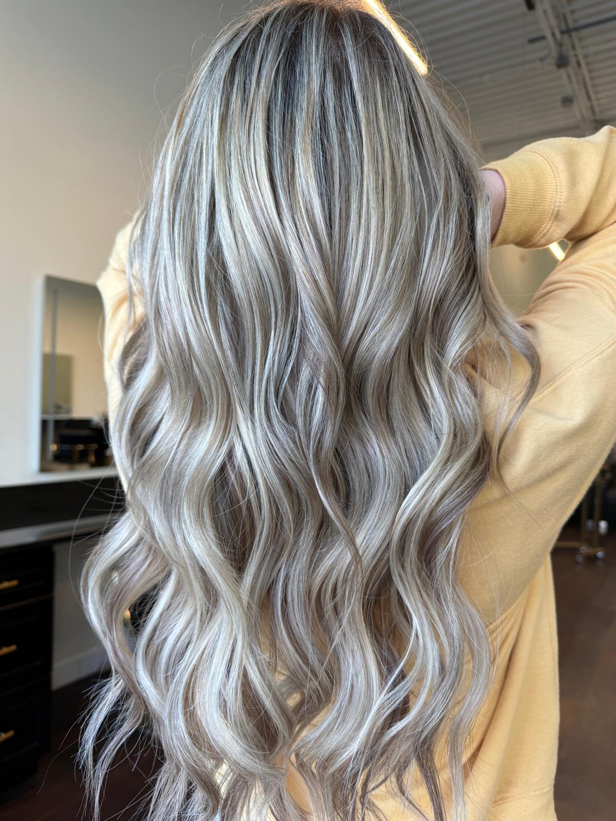 Long wavy ash blonde hair with soft highlights, seen from behind at Lumina Extensions & Beauty Bar, Cary NC